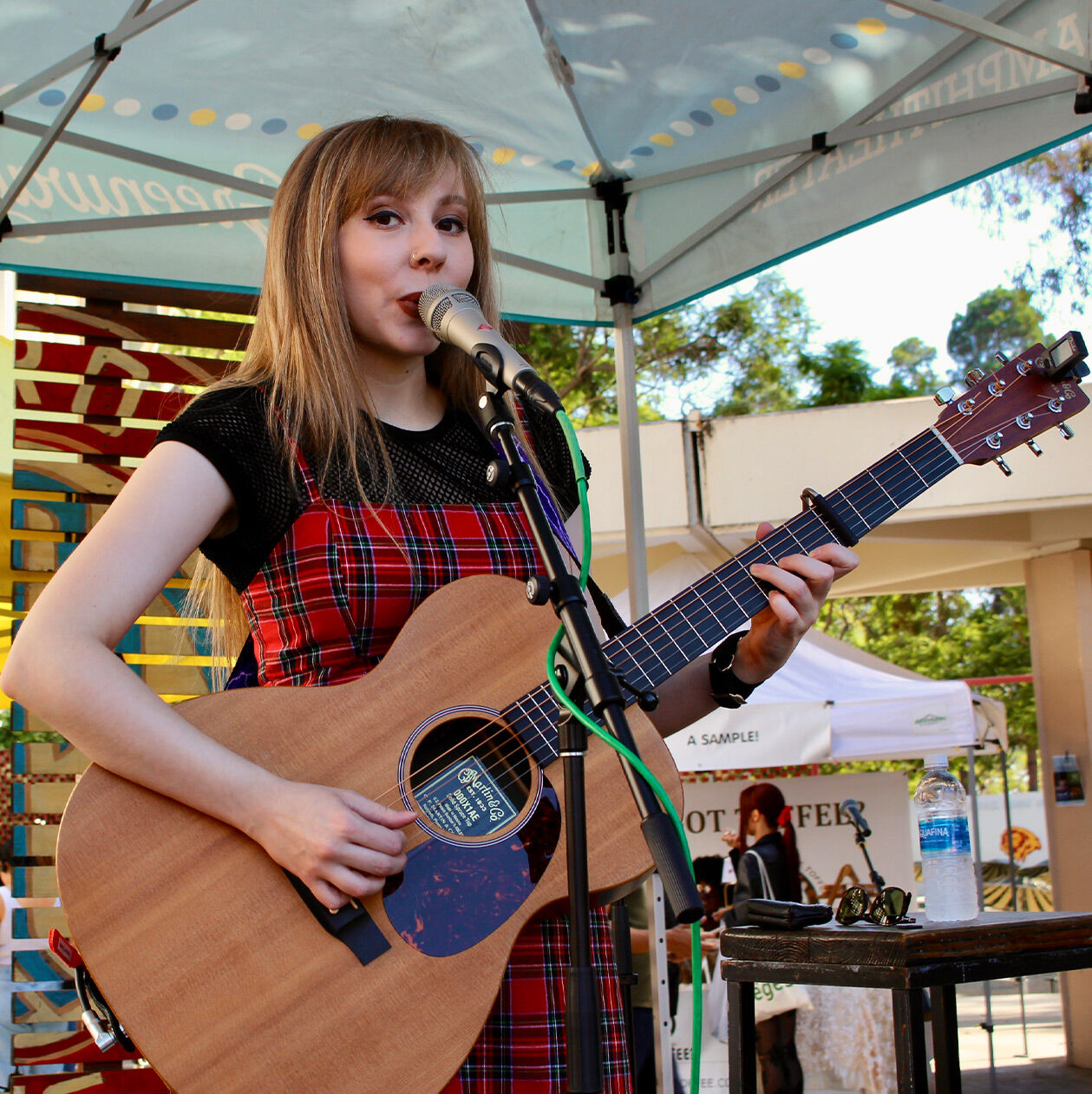 Abigail playing her acoustic guitar on a stage under a tent